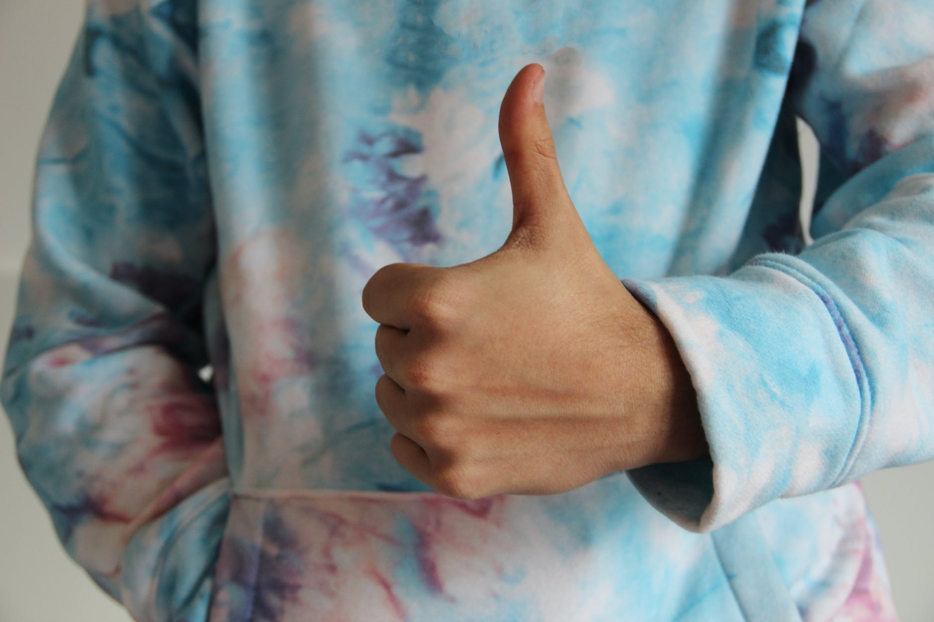 a person in tie dye sweater doing thumbs up